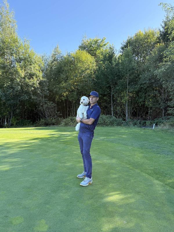 Bobby Bastviken i golfklær på greenen på Haga, med en liten hvit hund på armen